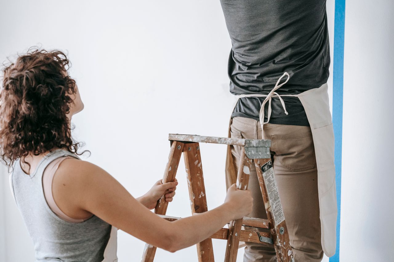 our-story-01 Couple working together to paint a wall during home renovation, featuring teamwork and DIY spirit.